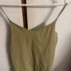 Beige ribbad linnetopp i ekologisk bomull - Säljer ett grönt  linne från Cubus i ekologisk bomull. Toppen har smala axelband och v-ringad halsringning. Perfekt för varma dagar eller som lager under andra plagg.