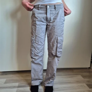 Gråa cargobyxor - Säljer ett par gråa cargobyxor med flera stora fickor på sidorna och bak. Byxorna är lowrise. Coola och trendiga.