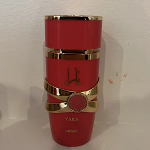Yara by lattafa (candy) - Yara parfym från Lattafa i en snygg Mörk rosa flaska med gulddetaljer och arabiska inskriptioner. Flaskan har en unik form med dekorativt guldband och Lattafa-logga. Perfekt för sommaren och sprejas på med andra olika sommar dofter! Har sprejats cirka 5 gånger.