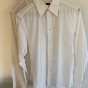 Vit skjorta från Spion - Klassisk vit skjorta från Spion i storlek 39. Skjortan har lång ärm, knappar framtill och en stilren krage. Perfekt för dig som gillar en enkel och tidlös look. Materialet känns lätt och passar till många tillfällen. 2 st för 150kr