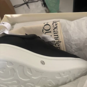 Svarta sneakers från Alexander McQueen - Säljer ett par svarta Alexander McQueen sneakers med vit, chunky sula och guldfärgad logga på hälen. Skorna har rund tå och klassisk snörning. Perfekta för dig som gillar stilrena och exklusiva sneakers.