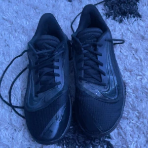 Svarta Nike sneakers med snörning - Säljer ett par svarta Nike sneakers med klassisk snörning och rund tå. Skorna har en sportig design med diskreta detaljer och platt sula, perfekta för träning eller vardagsstil.