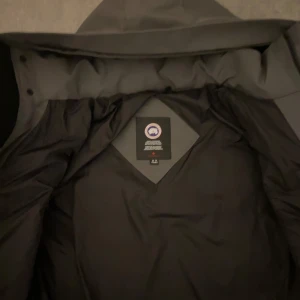 Grå parkajacka med pälsdetalj - Säljer en grå parkajacka från Canada Goose i storlek M. Jackan har en avtagbar pälsdetalj på huvan och är perfekt för kalla vinterdagar. Den är i mycket bra skick och har en klassisk design med långa ärmar och dragkedja framtill. Perfekt för både stad och natur!