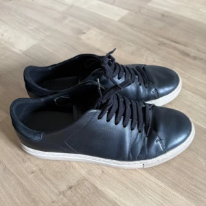 Axel Arigato clean 90 sneakers  - Stilrena svarta sneakers från Axel Arigato med vita sulor och svarta skosnören. Ovandelen är i skinn och bakkappan i mocka. Klassisk rund tå och platt sula. Perfekta för en clean och modern look.