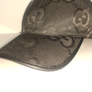 Svart keps från Gucci med GG-mönster - Snygg svart keps från Gucci med det klassiska GG-mönstret över hela kepsen. Justerbar rem baktill i skinn och insida i bomull. Perfekt accessoar för en trendig look.