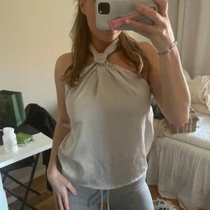 Beige halterneck linnetopp - Säljer en beige halterneck linnetopp med knytning i nacken. Toppen har en lös passform och är ärmlös, perfekt för varma dagar. Enkel och stilren design som passar till mycket.