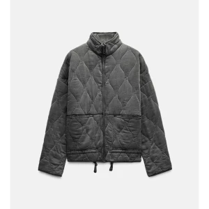 Grå quiltad jacka med dragkedja - Säljer en grå quiltad jacka med hög krage och dragkedja framtill. Jackan har långa ärmar, två stora fickor och justerbar dragsko nedtill. Perfekt för kyliga dagar och enkel att matcha med olika outfits.