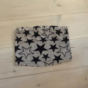 Grå tubtop med svarta stjärnor från Dazy - Grå tubtop från Dazy med svart stjärnmönster. Den har resår i midjan och är tillverkad i ett mjukt material som känns bekvämt. Perfekt för dig som gillar en lekfull och trendig stil.