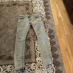 Grå jeans från Nudie Jeans - Säljer ett par grå jeans från Nudie Jeans med klassisk femficksdesign och snygga detaljer på bakfickorna. Byxorna har normal passform och raka ben. Perfekta för dig som gillar stilrena och tidlösa jeans. Kan gå ner i pris vid snabb affär.