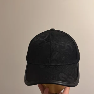 Gucci keps - Snygg svart keps från Gucci med diskret GG-mönster över hela kepsen. Justerbar rem baktill i svart och böjd skärm. Tillverkad i ett slitstarkt material med en stilren look.