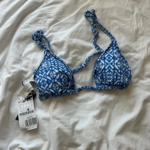 bikini överdel från stradivarius  - Säljer en blåvit bikiniöverdel från Lindex med knytbara axelband och ett mönster i blått och vitt. Triangelformade kupor och justerbara band för perfekt passform. Perfekt för stranden eller poolen!