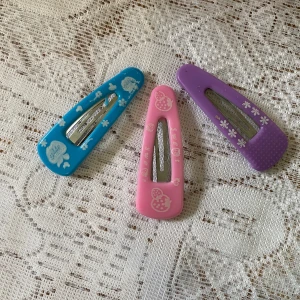 Färgglada hårspännen med mönster - Tre hårspännen i blått, rosa och lila med söta blommor och figurer. Perfekta för att piffa upp frisyren med en lekfull touch.