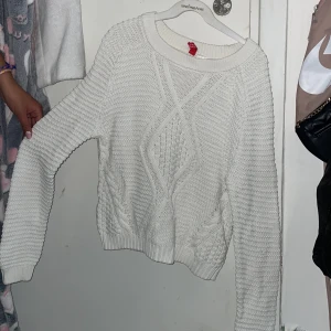 Vit stickad tröja från Divided - Säljer en vit stickad tröja från Divided med kabelstickat mönster framtill. Tröjan har rund halsringning och långa ärmar. Perfekt för lager-på-lager och passar till många olika stilar.