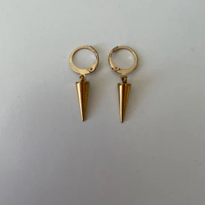 Guldiga örhängen med konformad hängande detalj - Säljer ett par handgjorda guldörhängen. Rostfritt material och nickelfria.