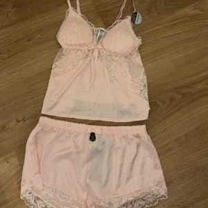 Ljusrosa spetspyjamas  - Säljer ett ljusrosa linne & ett par matchande pyjamas shorts. De har spets detaljer och är ljusrosa. De är i satin material. Jätte sköna på sommaren. De båda är i storlek s men kan absolut används av xs också. Helt nya. Inga hål eller fläckar och aldrig använda.