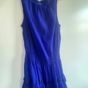 Blå klänning med volang - Säljer en blå klänning med plisserat tyg och volangdetaljer nertill. Klänningen har markerad midja med smock och en luftig känsla, perfekt för varma dagar. Jag säljer denna för att den aldrig används.