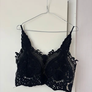 Svart spetsig topp - Säljer en svart topp med vackra spetsdetaljer och tunna axelband. Superfin att ha under en skjorta eller kavaj eller över bikini eller T-shirt. Sitter bra på mig som brukar bära S/M. Tveka inte på att höra av dig vid frågor eller prisförslag!