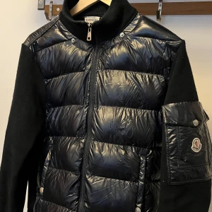 Svart pufferjacka från Moncler - Säljer en svart pufferjacka från Moncler med glansig framsida och ärmar i mjukare material. Jackan har dragkedja, ribbad krage och Moncler-logga på ärmen. Perfekt för kyliga dagar och riktigt snygg streetstil. Man kan scanna qr coden med