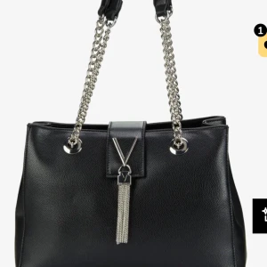 Svart handväska med kedjerem och tofsdetalj - Svart valentino väska, kan användas som skol väska då den får plats med skol material men även till annat. Fick väskan i julklapp men knappt använt 