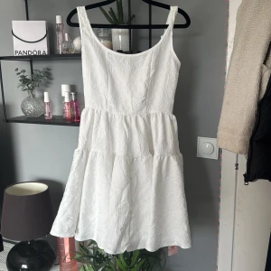 Vit ärmlös klänning från SHEIN MOD - Superfin vit klänning från SHEIN MOD med ärmlös design och lätt struktur i tyget. Klänningen har en rundad halsringning och voluminös kjol med flera lager, perfekt för varma dagar. Prislapp kvar 