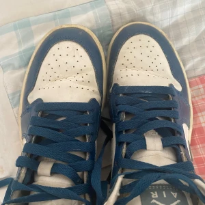 Nike Air Jordan 1 blå och vita sneakers - Säljer ett par Nike Air Jordan 1 sneakers i blått och vitt. Skorna har klassisk snörning, rund tå och är tillverkade i skinn. Perfekta för dig som gillar streetwear och vill ha en ikonisk modell i garderoben.