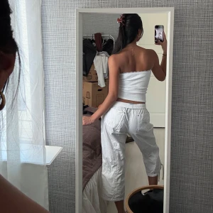 Vita cargopants med snörning - Säljer ett par vita cargopants med dragsko i midjan och flera fickor. Byxorna är trekvarts-långa och har en loose passform, perfekta för en avslappnad stil. Superbekväma och lätta att matcha med olika toppar.