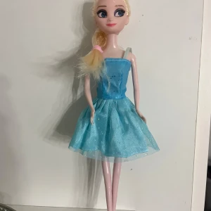 Elsa docka  - Super söt elsa docka i fint skick köptes med den här klänningen däremot har axelremen på klänningen låssnat (se bild) håret är om flätat och skor fattas annars är allt bra ❤️