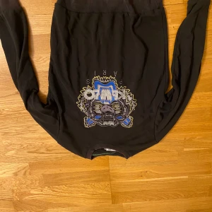 Svart sweatshirt med broderad tiger från Kenzo - Säljer en svart sweatshirt från Kenzo med en stor, färgglad broderad tiger på bröstet. Tröjan har rund hals och långa ärmar. Perfekt statement-plagg för dig som gillar unika detaljer.