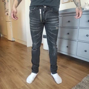 Svarta jeans med dragkedja - Snygga svarta jeans från Dsquared2 med slitna detaljer och en unik dragkedja framtill. Jeansen har en tight passform och är perfekta för en trendig look. De har också en cool tvättad effekt som ger extra stil.