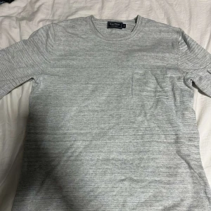 Grå långärmad tröja från Easy West - Säljer en stilren grå långärmad tröja från Easy Wear. Tröjan har en diskret bröstficka och är perfekt för en avslappnad look. Den är tillverkad i ett mjukt material som känns skönt mot huden.