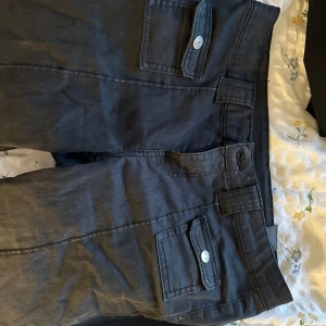 lowwaist cargojeans - Snygga svarta byxor med fickor och knappar framtill. Byxorna har en rak passform och är perfekta för en stilren look. De har en klassisk design med bälteshällor och knappstängning långa, storlek 40 men skulle säga typ som S är stretchiga. .