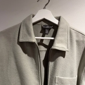 Beige fleecejacka från H&M - Säljer en stilren beige fleecejacka från H&M. Jackan har en dragkedja framtill och praktiska fickor. Perfekt för kyliga dagar.