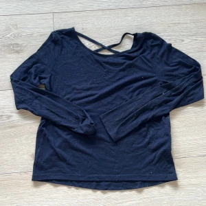Glittrig mörkblå långärmad topp med korsdetalj - Snygg glittrig mörkblå långärmad topp med korsdetalj vid nacken. Perfekt för en stilren look. Tillverkad i mjukt material för extra komfort.🩷🩷