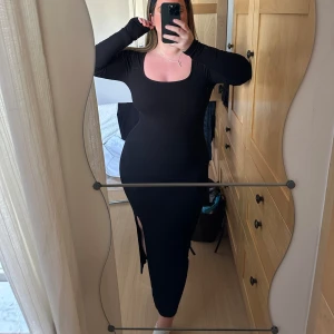 Svart långklänning med slits - Snygg svart ribbad långklänning med en slits på sidan. Klänningen har en tight passform och långa ärmar, perfekt för en elegant look. Den är ribbad vilket ger en fin textur och stil.