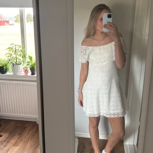 Vit spetsklänning - Säljer en söt vit spetsklänning med offshoulder-design och volangdetaljer. Klänningen har en öppen rygg och är perfekt för skolavslutning eller student! Är i storlek 164 men passar mig som vanligtvis har storlek S/M