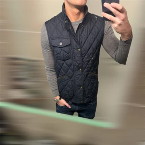 Ralph Lauren Väst  - Snygg blå quiltad väst från Polo Ralph Lauren med knappar och en bröstficka. Perfekt för lager-på-lager under kyliga dagar. Klassisk design med en modern touch. 
