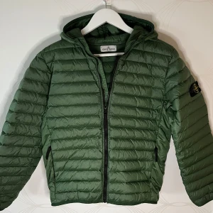 Stone Island dunjacka - grön - Jackan är inköpt år 2024 på NK (kvitto finns) och är knappt använd. I mycket fint skick! Nypris 5099 kr.                                                               ’                                                                            Perfekt nu till hösten – lätt vaderad, snygg och skön!                                                                           Hör av dig vid intresse, priset är förhandlingsbart.