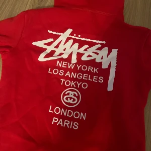 Stüssy hoodie - Säljer en snygg röd hoodie från Stussy med tryck, Fin hoodie som knappast är använd, köpt på impala streetwear malmö, går att användas av både tjejer/killar  Pris går att diskutera 🤗
