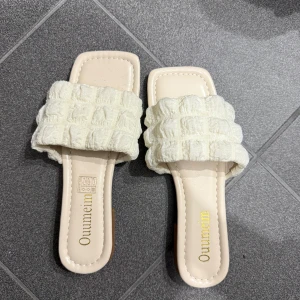 Beige sandaler med quiltad rem - Snygga beige sandaler med en bred quiltad rem över foten. Perfekta för en avslappnad sommarlook. Den fyrkantiga tån ger en modern touch.