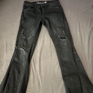 Svarta jeans med slitningar - Snygga svarta jeans med hål på framsidan. Byxorna har en bootcut-stil men är utsydda själv! Vet inte storleken men passar mig som har w 27