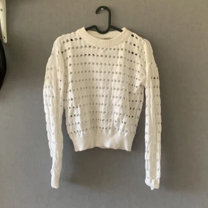 Vit stickad tröja från Samsa Young - Säljer en vit stickad tröja från Samsa Young med ett unikt hålmönster. Tröjan har långa ärmar och en rund halsringning. Perfekt för lager-på-lager-stil eller som ett statement-plagg i garderoben.