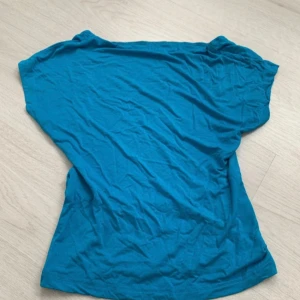 Turkos t-shirt med öppen rygg  - Säljer en turkos t-shirt med korta ärmar. Perfekt för en avslappnad stil. T-shirten har en enkel design och är tillverkad i ett mjukt material.