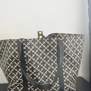 Mönstrad shoppingväska från By Malene Birger - Snygg shoppingväska från By Malene Birger med ett svart och vitt mönster. Väskan har svarta handtag och en praktisk storlek för alla dina behov. Perfekt för en dag på stan eller som en stilren accessoar.