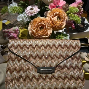 Glittrig kuvertväska från Teria Ybar - Snygg glittrig kuvertväska från Teria Ybar med ett zigzag-mönster i guld och brunt. Väskan har en elegant kedjerem och en praktisk dragkedja inuti. Perfekt för att ge din outfit en extra touch av glamour.