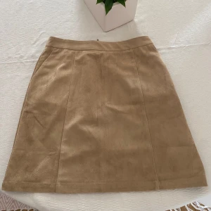 Beige kjol från NA-KD - Snygg beige kjol i mocka tyg från NA-KD i en klassisk stil. Kjolen har en dragkedja bak och är perfekt för en stilren look.