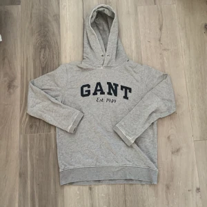 Grå hoodie från GANT - Säljer en klassisk grå hoodie från GANT med tryck framtill. *har en liten fläck på ärmen men syns inte när man har på den, barn size