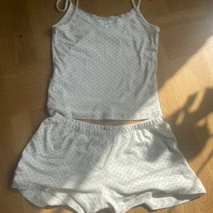 Gullig pyjamas från Brandy Melville - Mysig vit pyjamas med små blå blommor från Brandy Melville. Linnet har spetsdetaljer och smala axelband, medan shortsen har knappar framtill. Linnet går också såklart att styla till ett par jeans. Storlek xs-s.