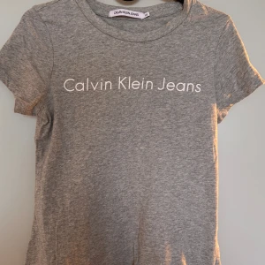 Grå Calvin Klein t-shirt - Säljer en äkta grå Calvin Klein t-shirt med vit logga på bröstet. Mjuk och väldigt bekväm. Använd endast ett fåtal gånger.