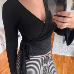 Svart omlottopp - Snygg svart omlottopp med långa ärmar och knytning i midjan. Perfekt för en stilren look.