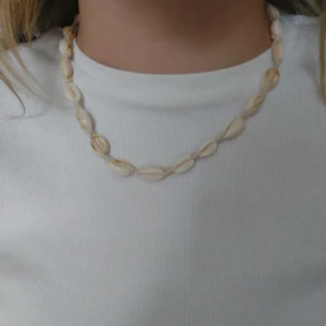 Halsband med snäckor - Snyggt halsband med vita snäckor knutna på ett justerbart snöre. Perfekt för en somrig look.